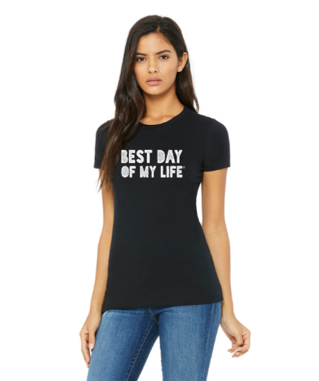 medium-skinned person with long brown hair wearing a fitted black crewneck t-shirt with best day of my life written across in white block lettering