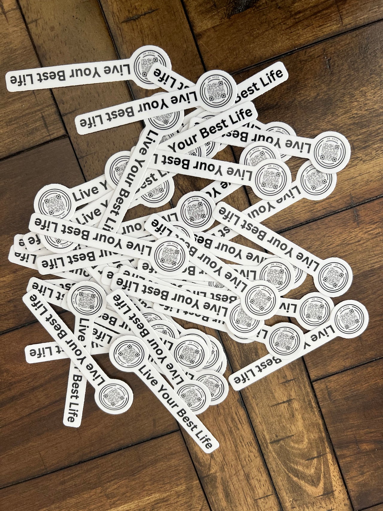 stack of stickers on wooden background, black text on white sticker has a qr code on the left and live your best life on right