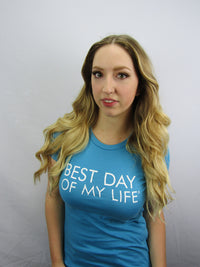 Thumbnail for light-skinned person with long, curled blonde hair wearing an aqua fitted crewneck tshirt with best day of my life written across in white.